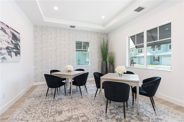 dining area with light wood-type flooring, a tray ceiling, visible vents, and baseboards