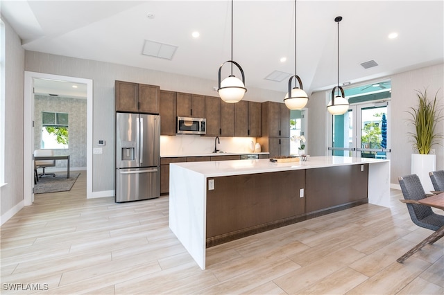 kitchen with lofted ceiling, a sink, light countertops, appliances with stainless steel finishes, and a large island