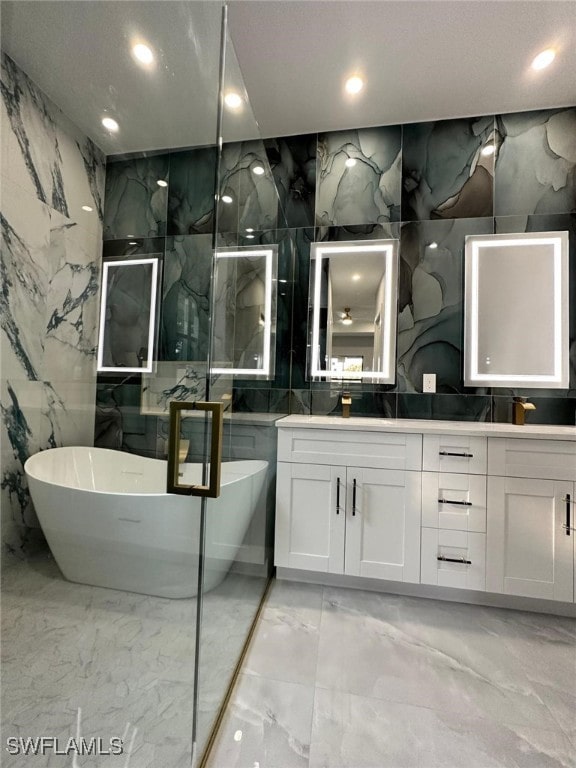 full bathroom with stone wall, tile walls, marble finish floor, a soaking tub, and double vanity