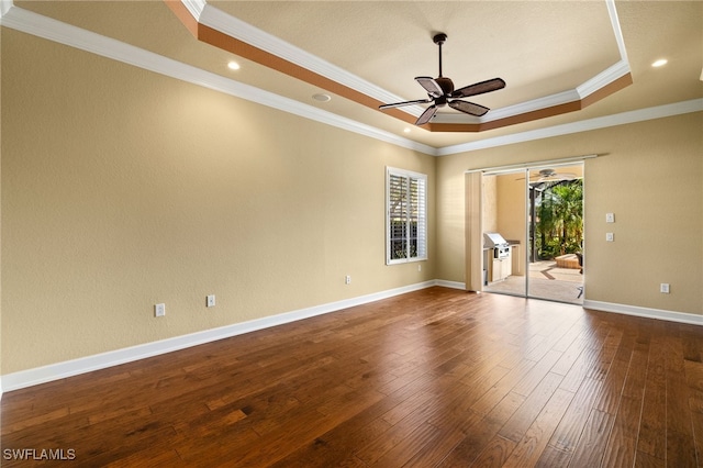 unfurnished room with baseboards, a raised ceiling, ceiling fan, dark wood-style flooring, and crown molding