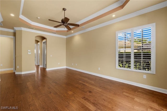 unfurnished room featuring baseboards, arched walkways, a raised ceiling, ceiling fan, and wood finished floors