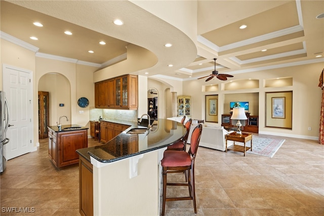 kitchen featuring arched walkways, brown cabinetry, an island with sink, a breakfast bar area, and a sink