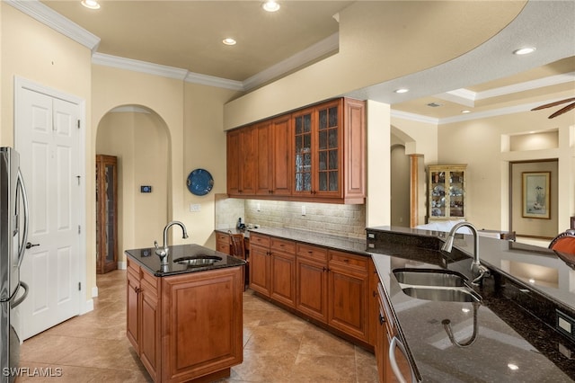 kitchen with arched walkways, brown cabinets, a sink, and dark stone countertops