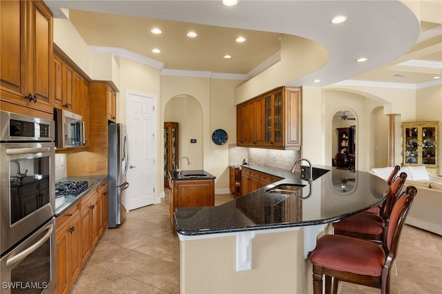 kitchen with appliances with stainless steel finishes, arched walkways, a sink, and a center island with sink