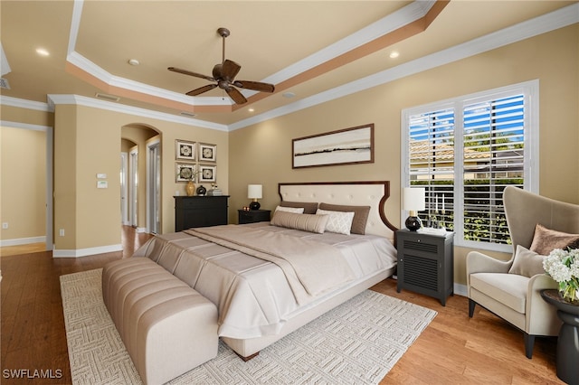 bedroom with light wood finished floors, a tray ceiling, arched walkways, and ornamental molding