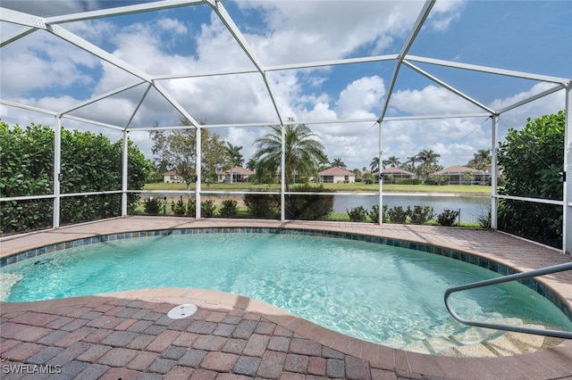 outdoor pool with glass enclosure, a water view, and a patio area