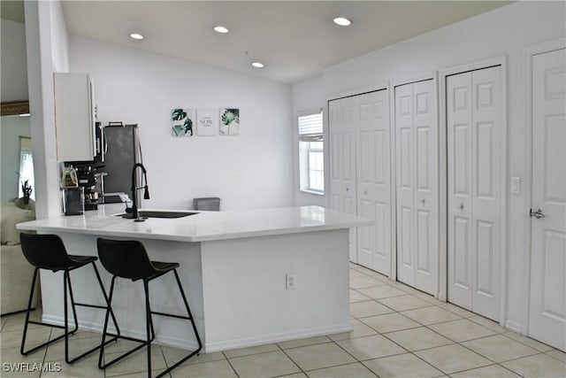 kitchen with a kitchen breakfast bar, a peninsula, light countertops, a sink, and light tile patterned flooring