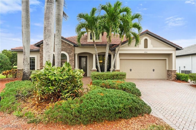 mediterranean / spanish house featuring decorative driveway, stone siding, an attached garage, and stucco siding