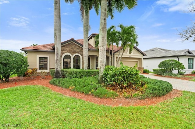 mediterranean / spanish home with a garage, a tile roof, decorative driveway, stucco siding, and a front lawn