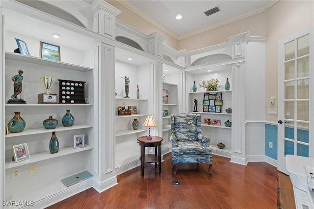 sitting room with built in features, visible vents, crown molding, and wood finished floors