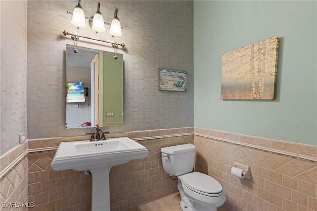 bathroom with wainscoting, toilet, and tile walls