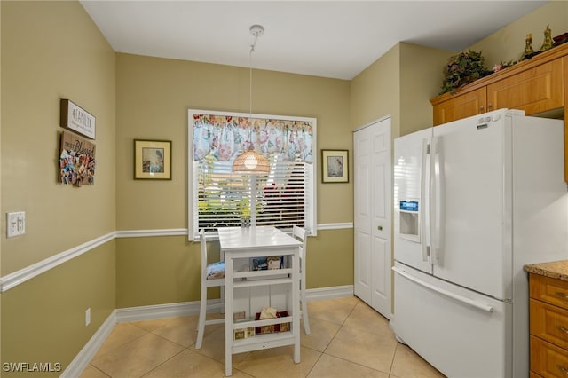 kitchen with white fridge with ice dispenser, brown cabinetry, light tile patterned flooring, and baseboards