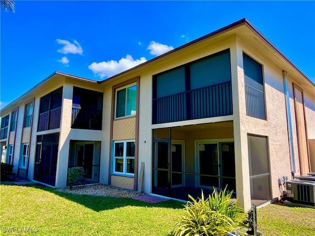 rear view of property featuring central air condition unit, a yard, and stucco siding