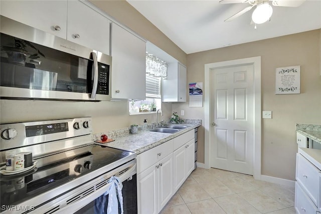 kitchen with light tile patterned floors, appliances with stainless steel finishes, white cabinetry, a sink, and baseboards