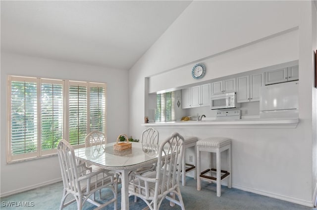 carpeted dining room with lofted ceiling and baseboards