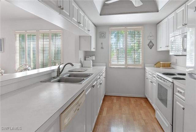 kitchen featuring white appliances, a raised ceiling, a sink, and white cabinets