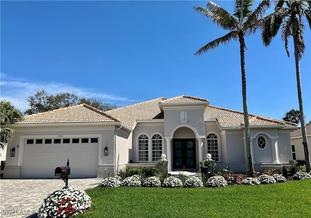 mediterranean / spanish home with a tile roof, an attached garage, decorative driveway, a front lawn, and stucco siding