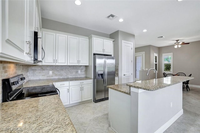 kitchen with stainless steel appliances, visible vents, white cabinetry, decorative backsplash, and an island with sink