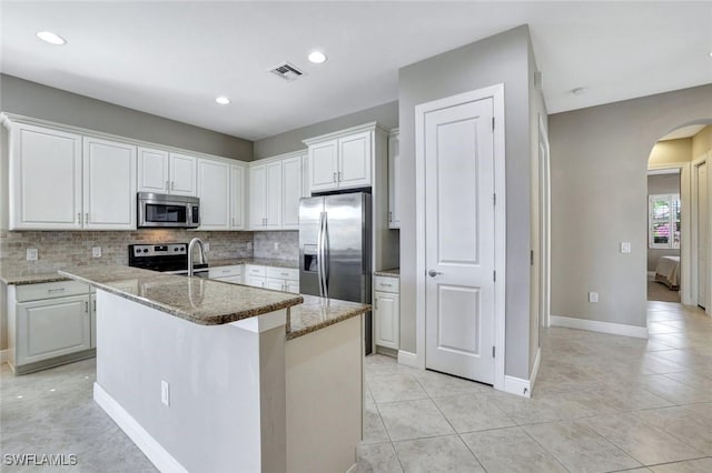 kitchen featuring arched walkways, stainless steel appliances, visible vents, decorative backsplash, and white cabinets