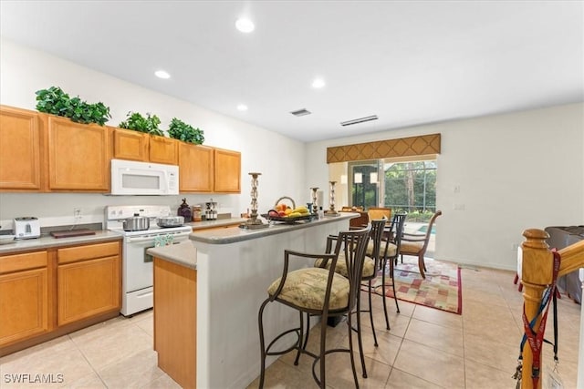 kitchen featuring white appliances, a kitchen island, light tile patterned floors, and a breakfast bar area