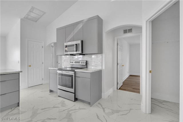 kitchen with arched walkways, gray cabinetry, stainless steel appliances, visible vents, and marble finish floor