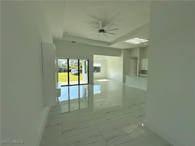 empty room with marble finish floor, a tray ceiling, a ceiling fan, and baseboards