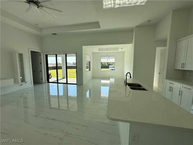 interior space featuring a sink, white cabinets, open floor plan, marble finish floor, and a tray ceiling