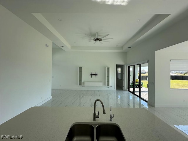 kitchen with a tray ceiling, open floor plan, a sink, ceiling fan, and baseboards