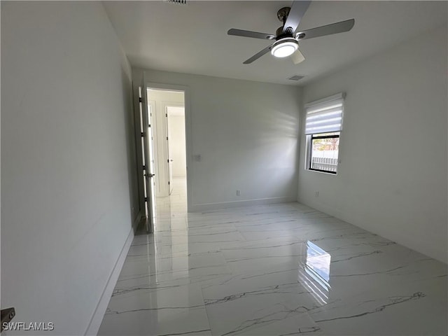 empty room with marble finish floor, visible vents, ceiling fan, and baseboards