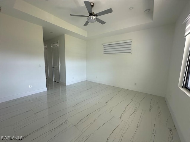 spare room with ceiling fan, marble finish floor, a raised ceiling, and baseboards