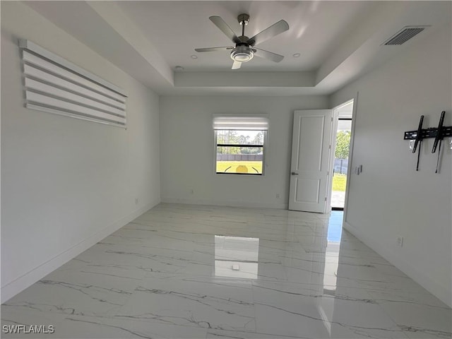 empty room with a tray ceiling, marble finish floor, ceiling fan, and baseboards