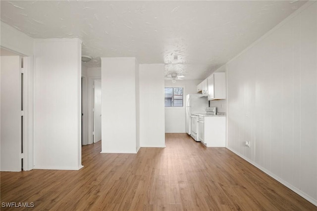 unfurnished living room featuring ceiling fan, light wood finished floors, and baseboards