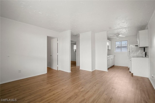 unfurnished living room featuring light wood-style floors, ceiling fan, a textured ceiling, and baseboards