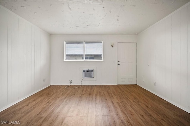 unfurnished room featuring a wall mounted AC, baseboards, and wood finished floors