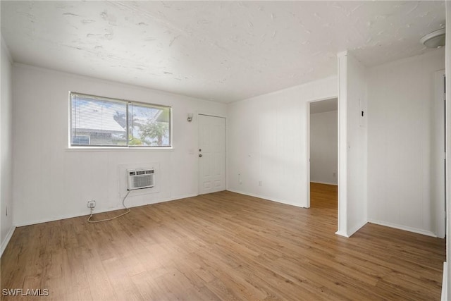 spare room with light wood-type flooring, baseboards, and a wall mounted AC