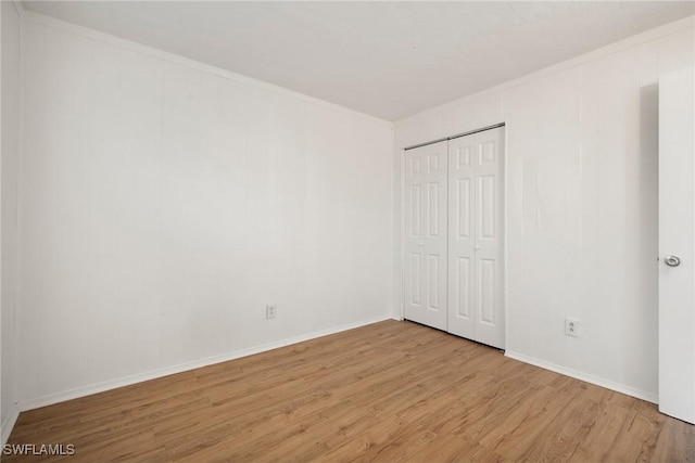 unfurnished bedroom featuring ornamental molding, a closet, baseboards, and wood finished floors