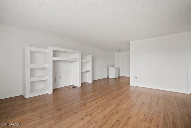 unfurnished living room with washer / dryer, built in shelves, light wood-style flooring, and a textured ceiling