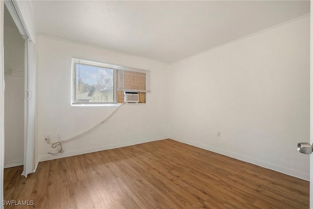 empty room with cooling unit, baseboards, and wood finished floors