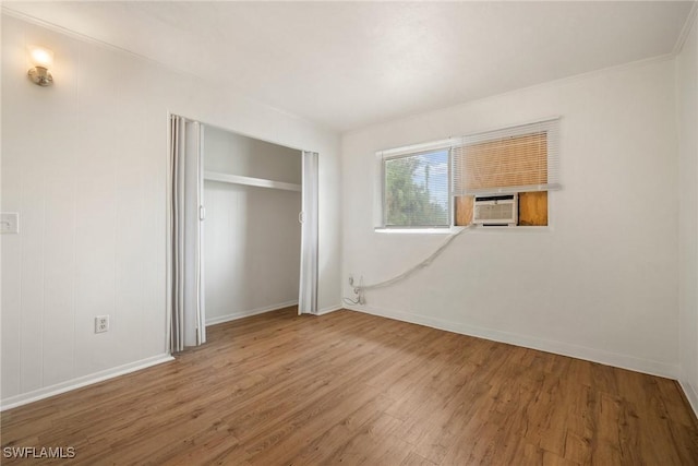 unfurnished bedroom featuring cooling unit, a closet, baseboards, and wood finished floors