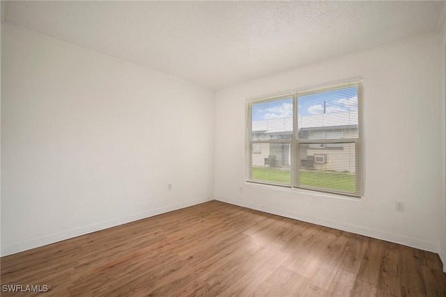 empty room with a textured ceiling, baseboards, and wood finished floors