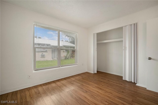 unfurnished bedroom with a textured ceiling, a closet, baseboards, and wood finished floors