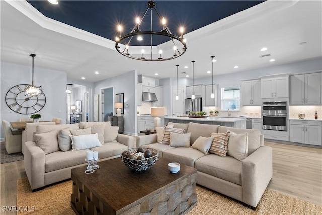 living room featuring a tray ceiling, visible vents, light wood-style floors, recessed lighting, and an inviting chandelier