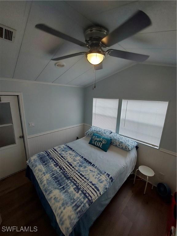 bedroom with dark wood-style flooring, visible vents, a ceiling fan, vaulted ceiling, and wainscoting