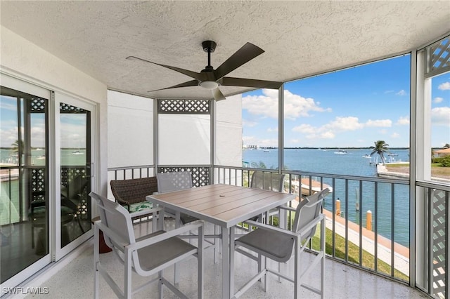 sunroom with plenty of natural light, a water view, and a ceiling fan