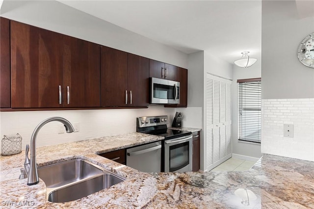 kitchen featuring light stone counters, light tile patterned floors, appliances with stainless steel finishes, dark brown cabinetry, and a sink