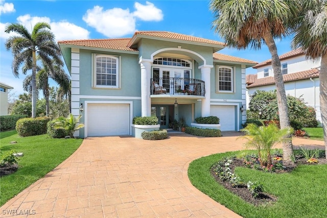 mediterranean / spanish-style house featuring a balcony, a garage, decorative driveway, and stucco siding