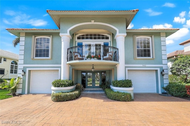 view of front facade with french doors, decorative driveway, an attached garage, and stucco siding