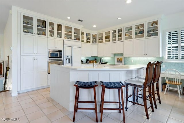 kitchen with a breakfast bar, white cabinetry, decorative backsplash, and built in appliances