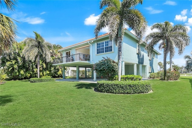 back of property with driveway, a lawn, a balcony, a carport, and stucco siding