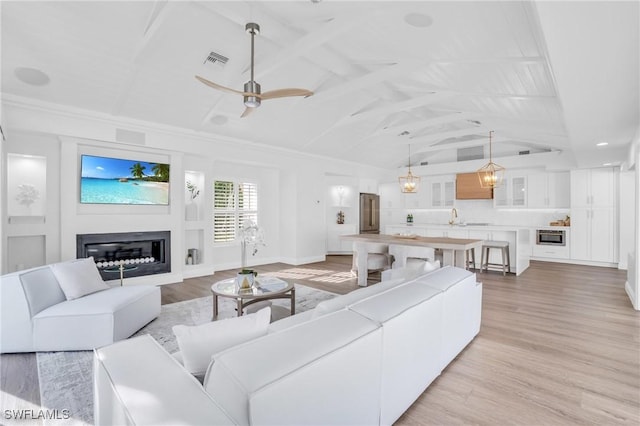 living area featuring light wood-type flooring, visible vents, vaulted ceiling, and a glass covered fireplace